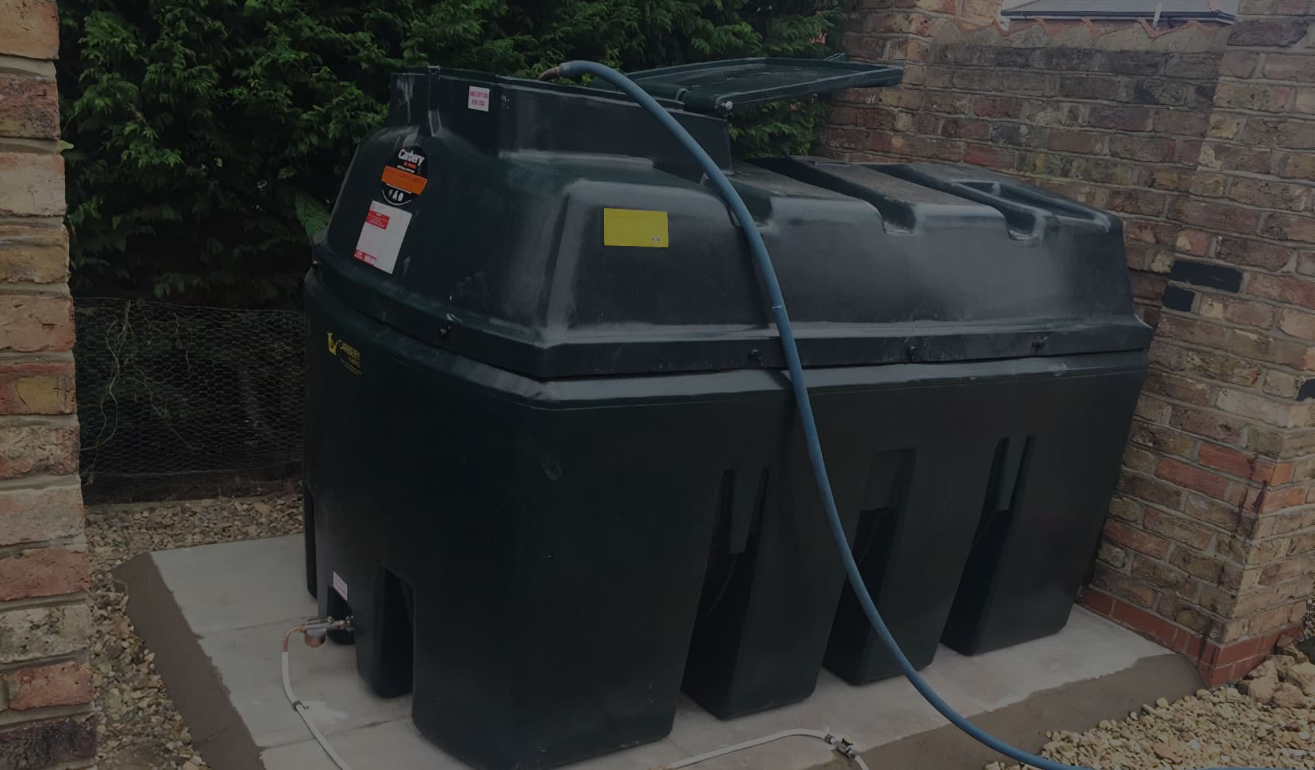 Green bunded oil tank installed on a paved base beside a brick property
